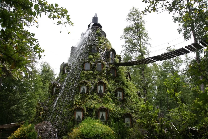 Exterior del Hotel Montaña Mágica cubierto de vegetación, con una pasarela sobre el bosque