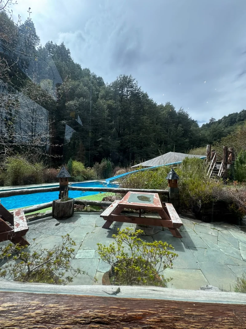 Piscina exterior de Termas Vergara junto a una mesa de madera y jardines