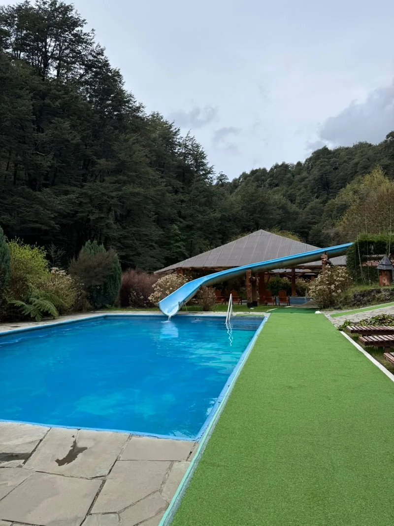 Piscina exterior de Termas Vergara con tobogán azul y jardines